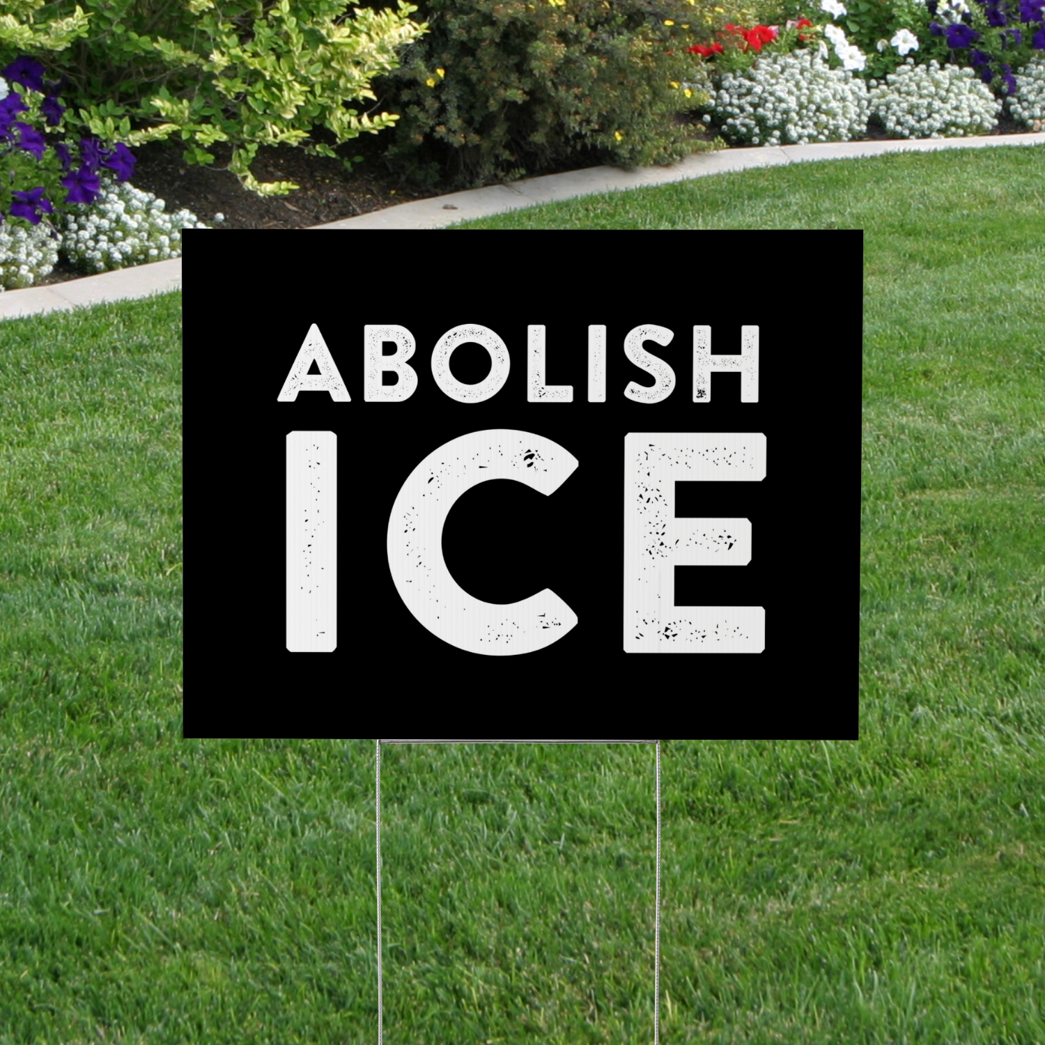 Garden sign with 'ABOLISH ICE' text on a grassy lawn