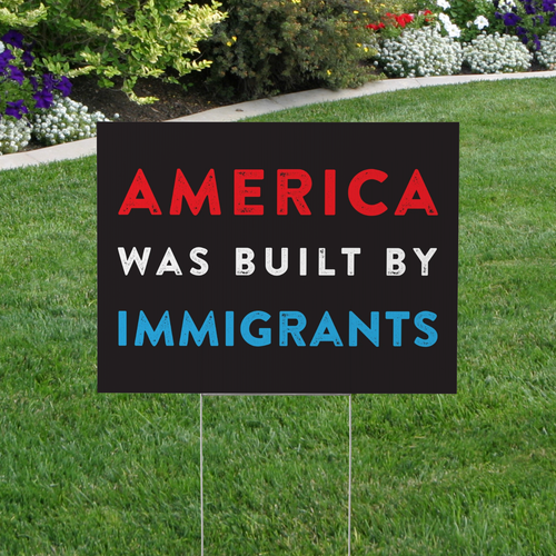 Garden sign with 'America was built by immigrants' text on a grassy lawn.