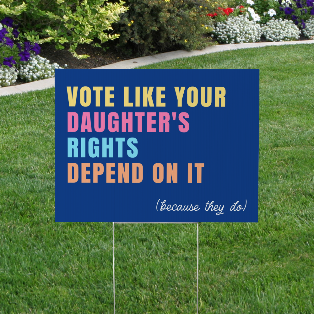 Blue political yard sign reading "Vote Like Your Daughter's Rights Depend On It (Because They Do)" displayed on a lawn