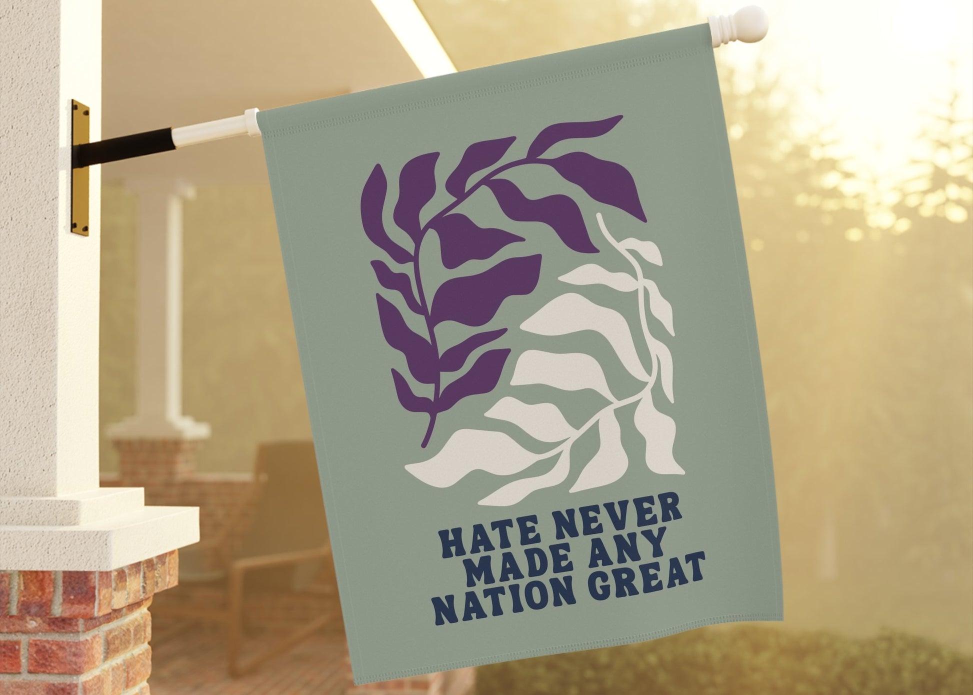 Flag with leaf design and text 'Hate never made any nation great' on a flagpole outdoors.