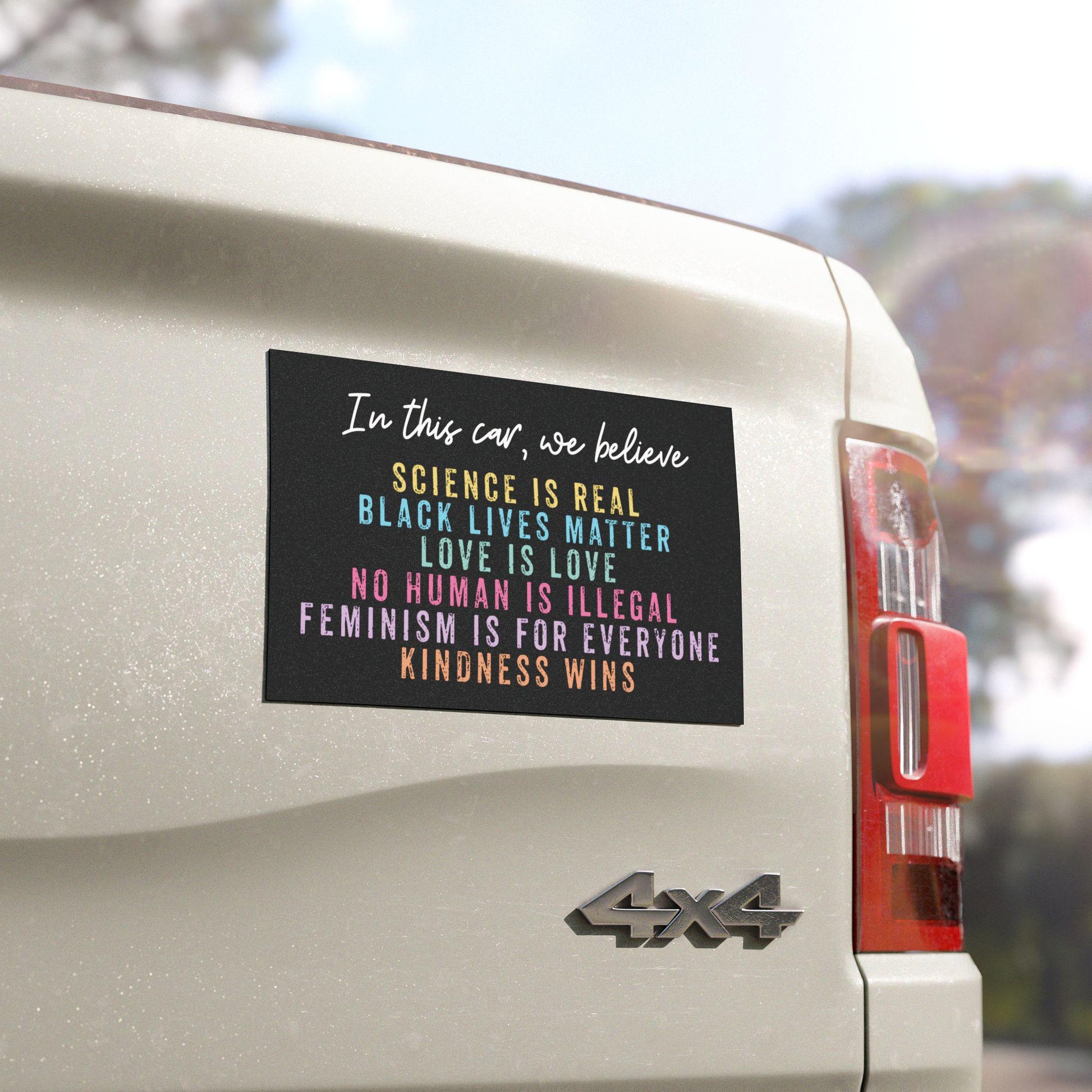 Black car bumper magnet with distressed block lettering that reads: “In this car, we believe: science is real, black lives matter, love is love, no human is illegal, feminism is for everyone, and kindness wins.”