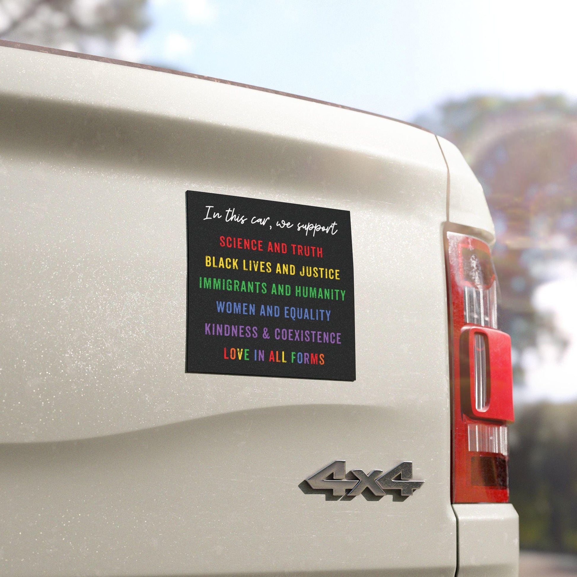 Magnet with the text “In this car, we support: science and truth, black lives and justice, immigrants and humanity, women and equality, kindness, unity and coexistence, love in all forms” on a rainbow background, displayed on a car bumper.