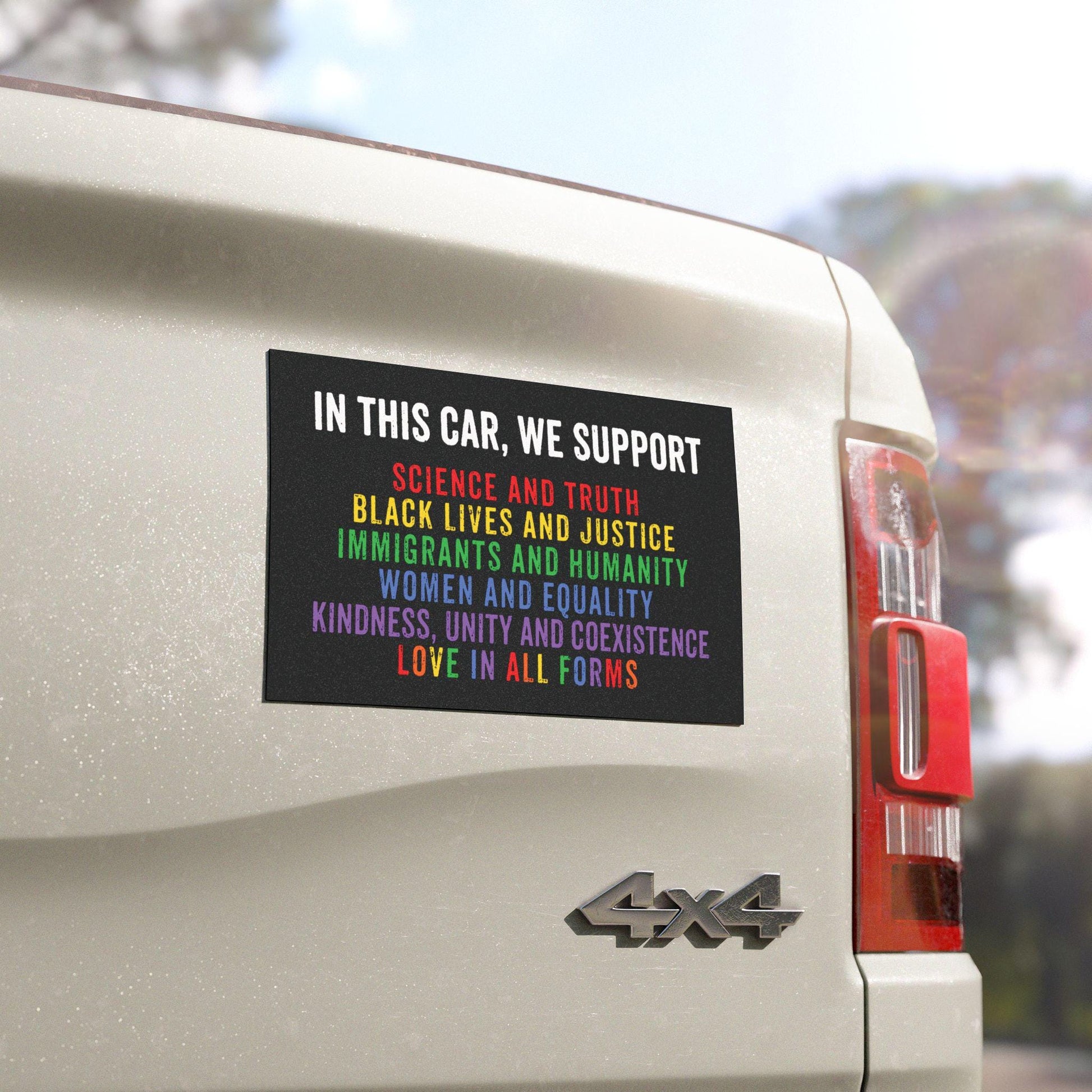 Magnet with the text “In this car, we support: science and truth, black lives and justice, immigrants and humanity, women and equality, kindness, unity and coexistence, love in all forms” on a rainbow background, displayed on a car bumper.