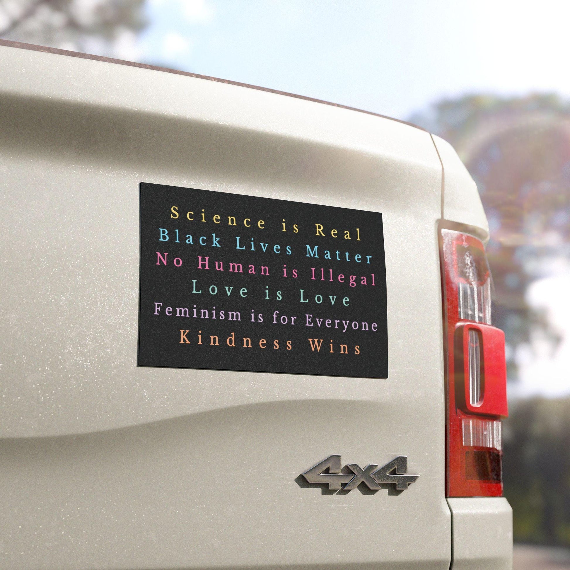 Rectangular car bumper magnet with black background and pastel text reading: “Science is real, Black Lives Matter, Love is Love, No Human is Illegal, Feminism is for Everyone, Kindness Wins.”