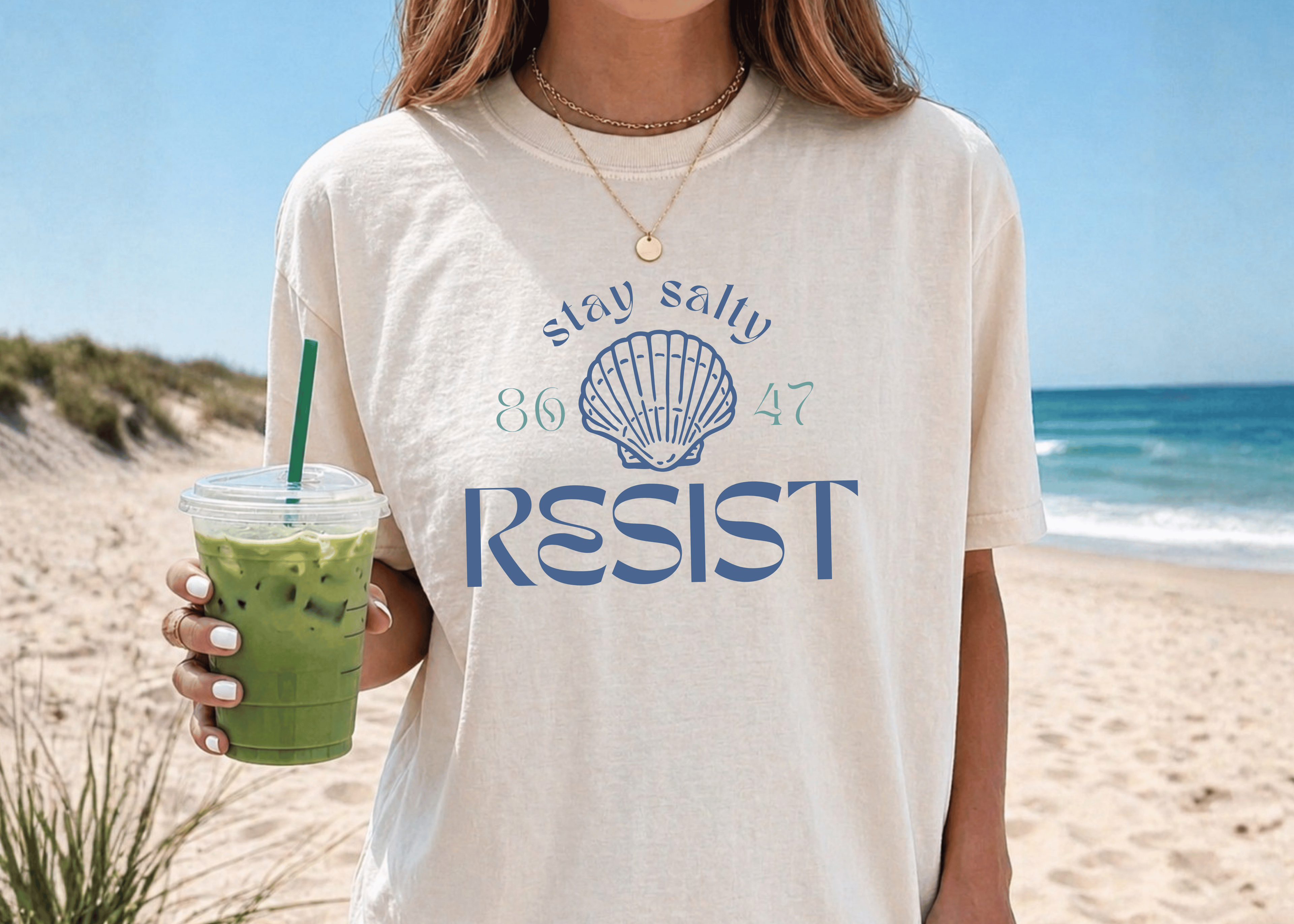 Person wearing a t-shirt with 'Stay salty 86 47 RESIST' design on a beach.